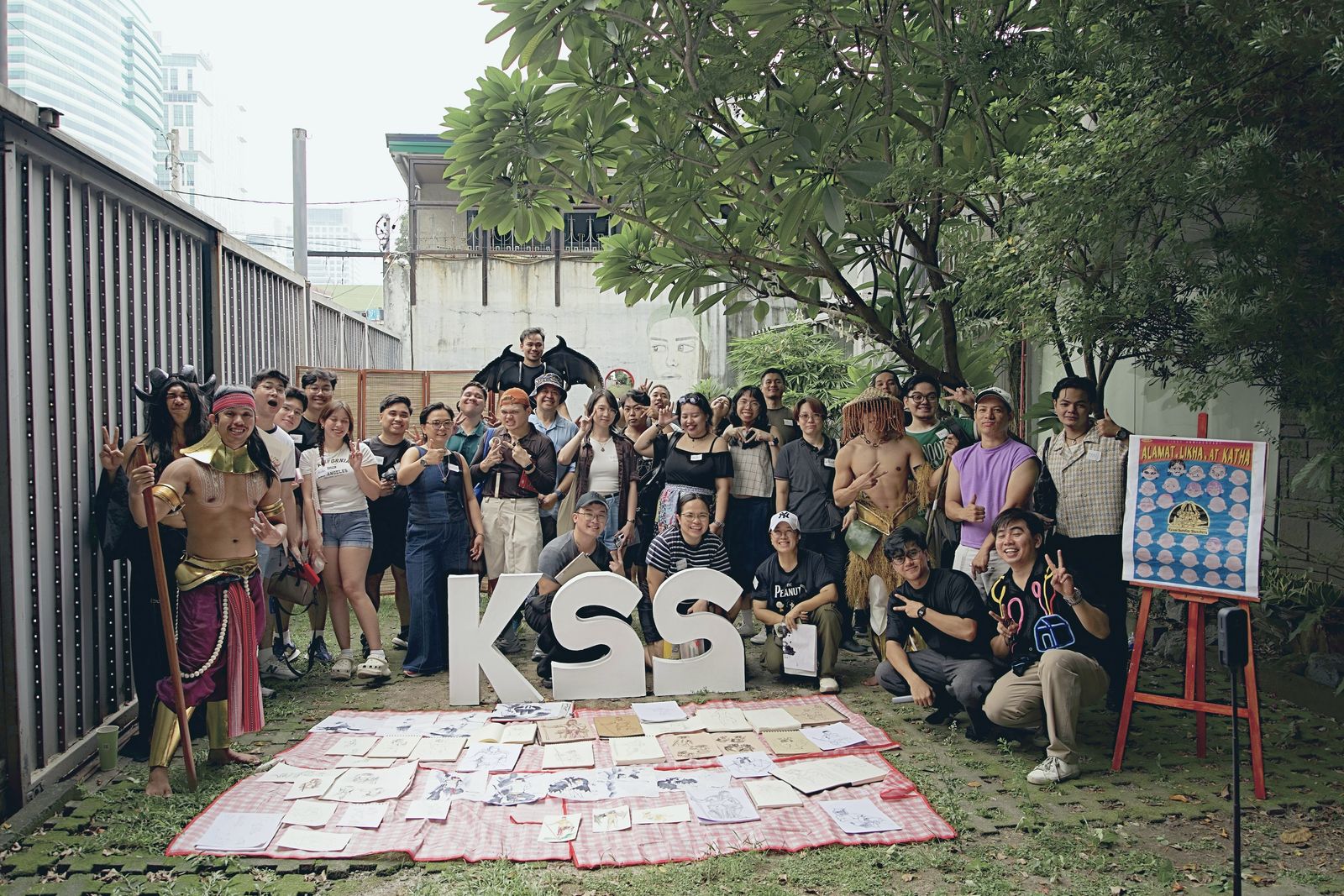 The KSS Vol. 8 group photo: artists and the three costumed models behind the drawings laid out on the mats, with the KSS letters in front